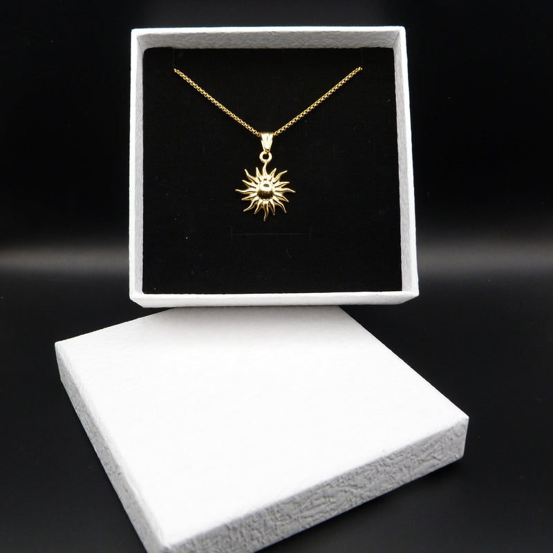Gold necklace with sun design in a black box on a dark background