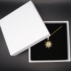 Gold sun-shaped necklace in a white jewelry box on a black background