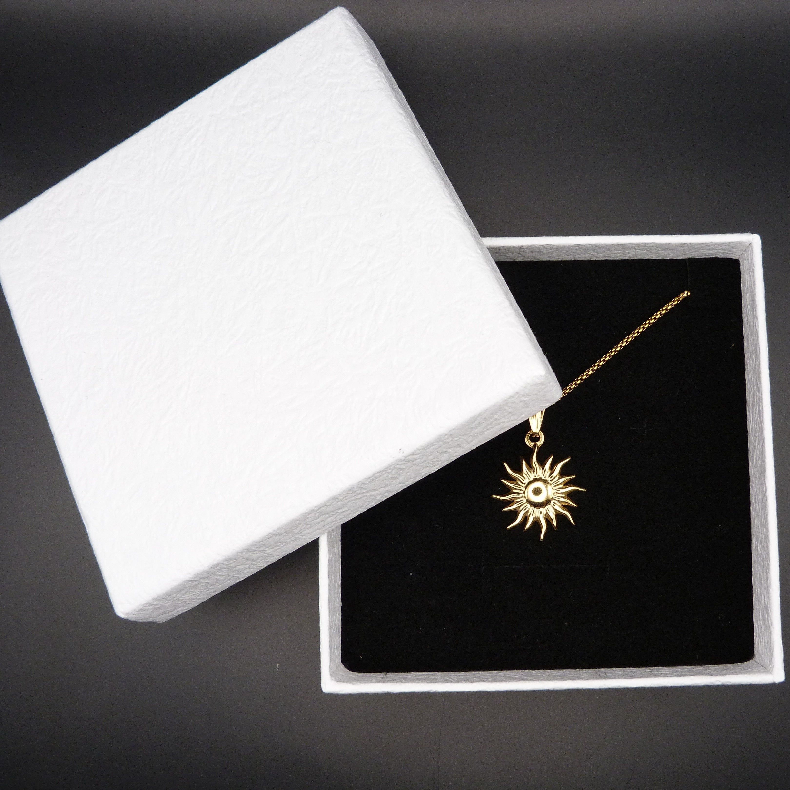 Gold sun-shaped necklace in a white jewelry box on a black background